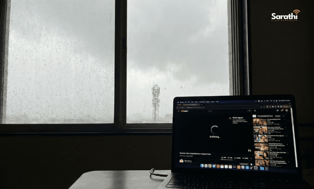 A laptop screen showing a buffering video during a heavy monsoon rain in Wagholi, with a cell tower visible outside the window.