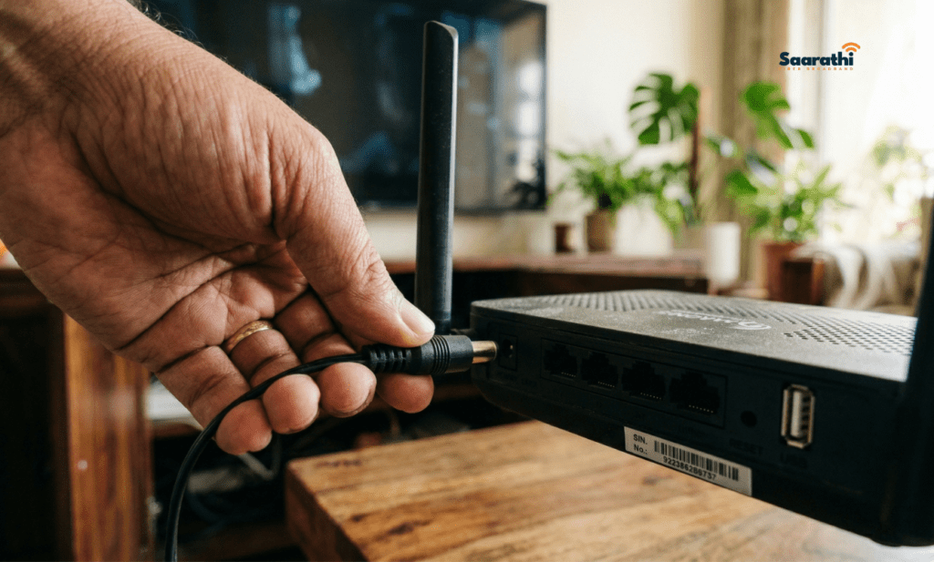 Hand unplugging the black power cable from the back of a wireless broadband router to restart it.